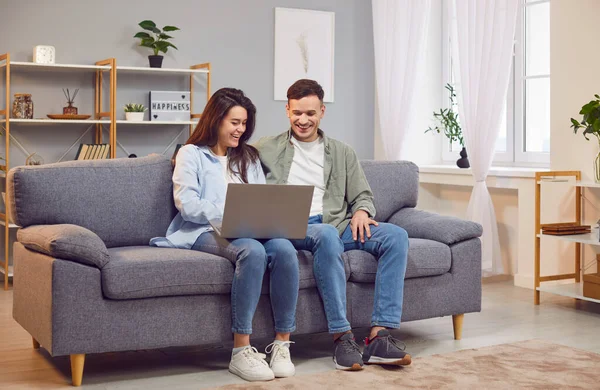Happy married couple enjoying leisure time together at home, using a laptop for online entertainment. Talking and laughing, moment of happiness and togetherness while engaging with the internet.
