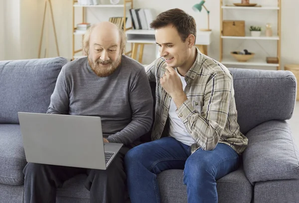 Elderly father and son spend online leisure together using a laptop at home, focusing on entertainment and family bonding in a cozy setting with a sense of relaxation and shared digital enjoyment.
