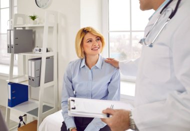 Caring male doctor comforting smiling patient in office. Closeup of therapist, general practitioner giving prescription and discussing treatment with blonde woman at visit. Medical support, healthcare