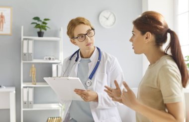 Female patient engages in a consultation conversation with a doctor or nurse in a hospital office. Healthcare advice, medical expertise, and patient support in a professional setting.