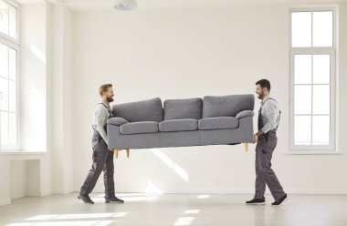 Delivering furniture, professional moving company team doing sofa transportation to empty home room, new office, two shipping company carrier workers together carrying couch, managing logistics 
