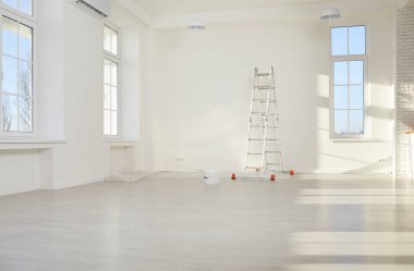Empty light modern room with white painted walls, step ladder and paint bucket standing in new apartment. Construction equipment for painting renovation process in house. Home repair concept.