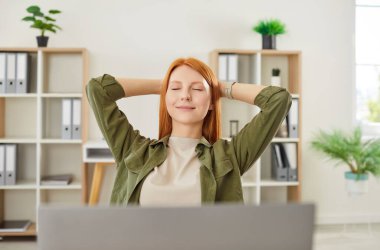 Portrait of a woman working online from home office, sitting at laptop and relaxing or resting as she leans back in chair. Taking a break while staying productive in a calm home space.