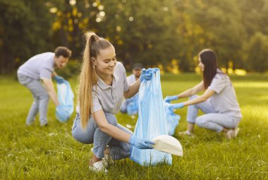 Group of happy volunteers participating in environmental clean up, working together in green park, picking up litter collecting garbage, friends community members actively engaging environment cleaner