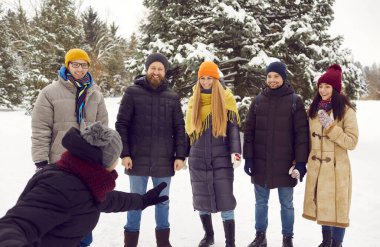 Smiling happy young people listen to funny story told to them by male friend during winter walk. Man cheerfully shows and tells story to his friends standing in front of him. Friendship and winter.