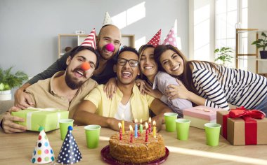 Group portrait of overjoyed millennial multiracial friends celebrate birthday make surprise. Smiling diverse multiethnic young people have fun enjoy anniversary celebration with cake and presents.
