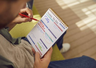 Not defterinde yazmakla meşgul bir adam. Elinde kalem ve üretkenlik planlayıcısı olan bir adam, iş görevlerini ve sorumluluklarını sayfa üzerine not ediyor ve tasarım şablonlarını hazırlıyor. Yakın çekim, yakın çekim.