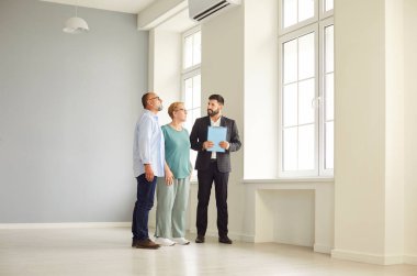 Realtor and agent guide a senior couple through new apartment during a tour and viewing, helping buyers assess the interior and showing key home features. Real estate market and buying property.