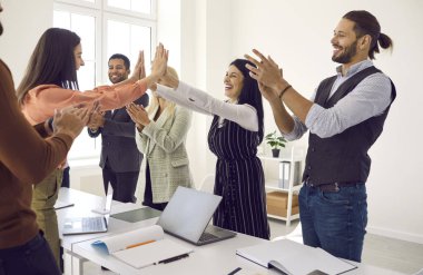 Çeşitli etnik çeşitlilikteki çok ırklı takım arkadaşları alkışlarken, konferans odasında ofis masasında duran ve birbirlerine beşlik çakan mutlu genç kadınlar. İş ekibi, takım çalışması, başarı konsepti