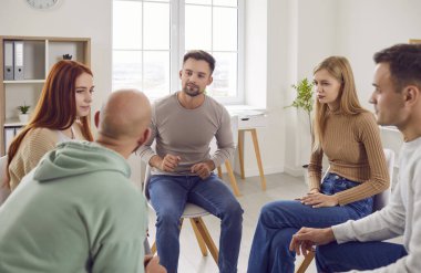 People communicating in group therapy. Adult men and women having psychotherapy session with professional therapist, sharing their issues and problems, talking about destructive feelings and emotions