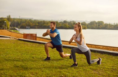 Aktif genç çift doğada esneme egzersizi yapıyor. Spor giyim kuşamında mutlu bir kadın ve erkek parkta spor yapıyor. Açık hava eğitimi ve spor konsepti.
