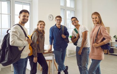 Portrait of smiling diverse multiethnic students with backpacks pose together in college or university classroom. Happy multiracial young people in high school. Education and diversity concept.