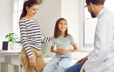 Pediatrician appointment. Preteen girl and her mom are talking to pediatrician during medical examination in hospital. Male doctor is listening to smiling child sitting on examination couch.