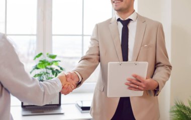 Close up of a happy businessman shaking hands with a client or colleague in the office. This handshake signifies a successful deal, partnership, or agreement, reflecting teamwork and collaboration.