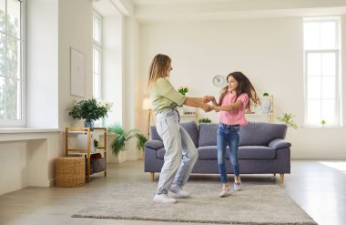 Mother and daughter dance, holding hands, smiling. They spin playfully with joy in a home livingroom. Soft carpet and simple decor set a cheerful, fun mood. Cheerful family connection and trust.