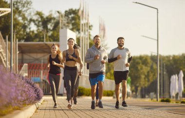 Group of young 30 sand sportive men and women jogging outdoors. Athletic people wear sportswear running in modern stadium during sunny summer morning or day. Healthy lifestyle, sport concept