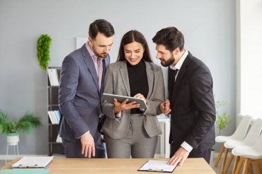 Company employees talking with colleagues standing workplace in office looking at tablet monitor screen discussing work projects. Young business people coworkers working at the desk having a meeting.