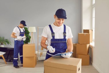 Yeni apartman dairesinde karton kutu teslimatında çalışan mutlu, genç ve profesyonel işçi takımı. Taşınma, taşınma günü ve taşınma konsepti.
