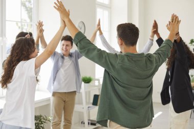 Group of happy diverse friends having fun at school. Several cheerful, smiling Caucasian and African American teenage boys and girl standing in a circle, holding hands and raising them up together