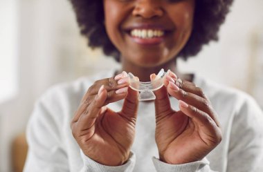 Happy, smiling young African American woman holding a teeth whitening tray. Close up of hands holding a plastic teeth tray for dental whitening like in a professional clinic. Oral care, beauty concept