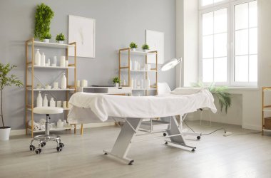 Clean, spacious cosmetology treatment room with professional treatment chair, modern equipment, and shelves stocked with skincare products, no people. Beauty clinic, spa interior designs concept
