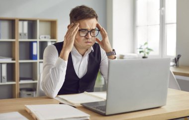 Frustrated young man looking laptop screen, feeling tired with business deadline, sad, annoyed, shocked reading bad news, busy male manager stressed at office work puffing cheeks, fingers on temples