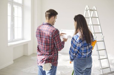 Backside view of a married couple reviewing a blueprint or draft together, planning the renovation of new home or apartment. Teamwork, construction goals, and shared vision for the project.