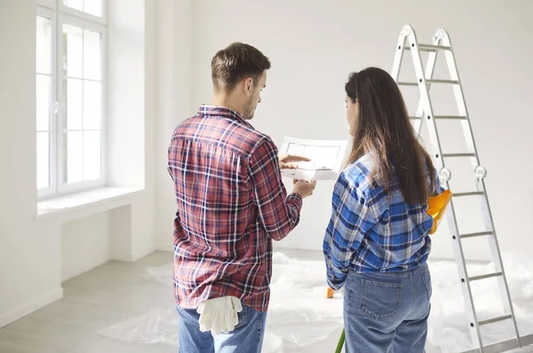 Backside view of a married couple reviewing a blueprint or draft together, planning the renovation of new home or apartment. Teamwork, construction goals, and shared vision for the project.
