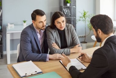Businesswoman and businessman sitting in real estates office at desk, having talk with agent, reading contract terms, listening different offers, having successful negotiations, making deal