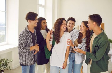 Group of happy smiling diverse friends in the classroom. Cheerful teenage multiethnic boys and girls meet after class, share news, discuss school and have fun together