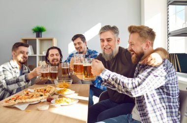 Gülümseyen sakallı erkek en iyi arkadaşlar bira ve pizzayla evde oturup eğleniyorlar ve gülüyorlar. Çekici, modern, pozitif erkeklerin portresi. Partide birlikte vakit geçirmekten zevk alıyorlar..