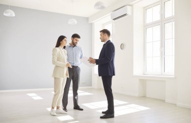Young married couple discussing contract with male realtor agent and looking through the documents going to buy a property. Family ready to become homeowners. Real estate market concept.