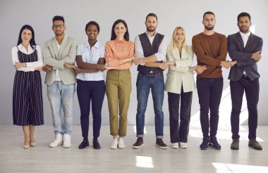 Çeşitli meslekdaşlar el ele tutuşup birlik ve destek gösteriyorlar. Genç erkekler ve kadınlar sırada el ele tutuşup kameraya bakıyorlar. Takım çalışması ve destek kavramı.