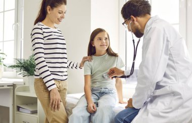 Mother and child come together to their family doctor. Pediatrician or family practitioner puts stethoscope to chest of happy little girl and listens to her lungs or heartbeat. Medical exam concept 