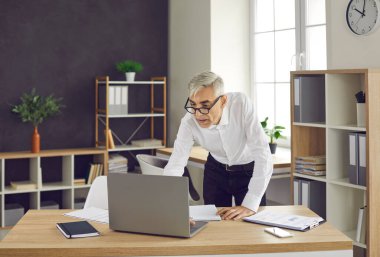 Concentrated senior European businessman while working with laptop computer in office, office lifestyle concept. A man in a white shirt and glasses at a laptop