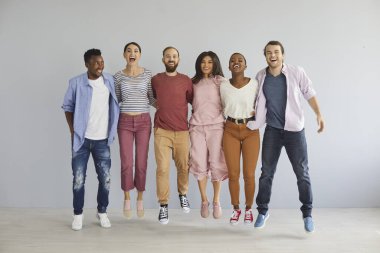 Diverse group of happy young people jumping in studio. Bunch of cheerful positive excited international multicultural mixed race college students in casual clothes jumping together and laughing