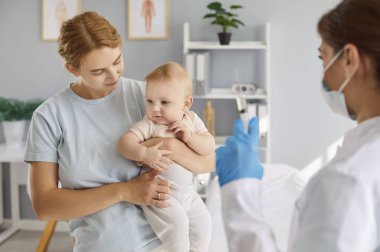 Mom holds cute 6 or 7 month old baby son or daughter for nurse practitioner to give flu, covid19, polio, hepatitis, diphtheria or tetanus inoculation jab. Child vaccination, illness prevention concept