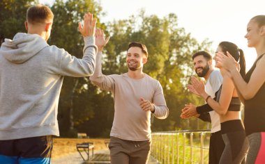 People high fiving and clapping, gathering outdoors in sunny park, support expressing joy and accomplishment, friends team participating in activity, positive success, teamwork physical celebratory 