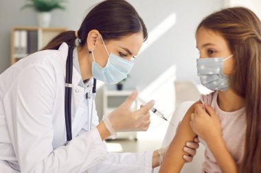Nurse in white gloves holding a syringe and giving a shot to a child. Doctor at a modern vaccination center gives a new effective Covid 19 vaccine injection to a little kid. Immunization concept