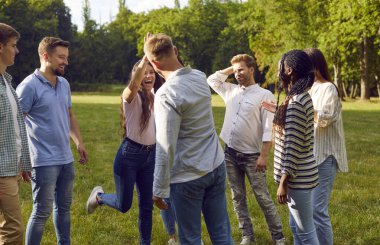 Cheerful group of best friends give each other high five while meeting in park. Multiracial men and women happy to see each other while walking in summer city park. Concept of friendship.