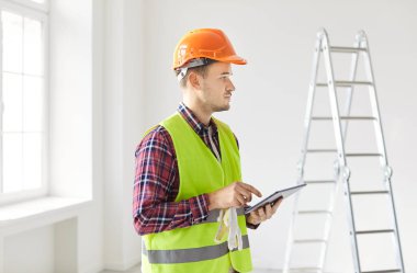 Concentrated male contractor or worker planing a renovation project using a tablet PC, reviewing blueprints and drafts while calculating an estimate for construction and project management.