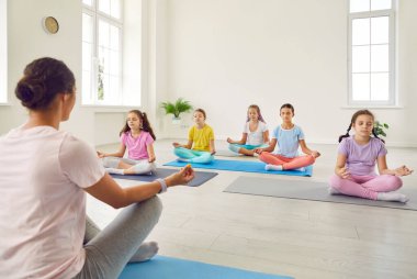 Group of kids having a yoga lesson. Children doing relaxing exercises. Little girls in sportswear sitting on the floor on mats in the lotus pose and meditating together with their teacher