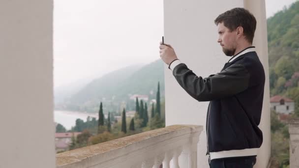 Mann fotografiert die Landschaft mit dem Handy, das er durch das Fenster sieht — Stockvideo