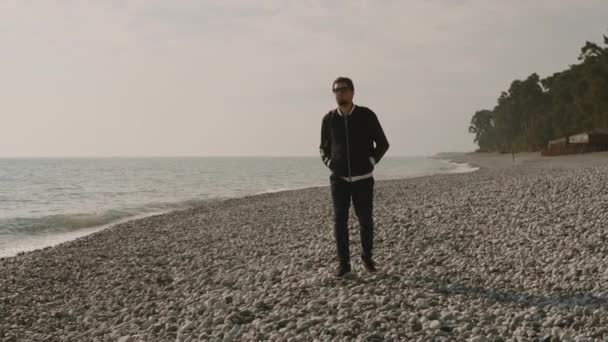 Ein einsamer Mann schlendert an einem steinigen Strand entlang, Wellen schlagen gegen das Ufer — Stockvideo