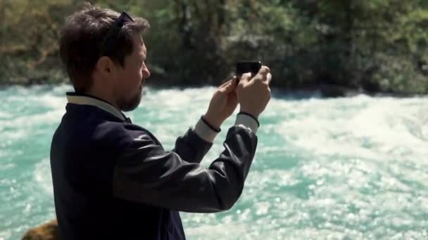 A young man holding a smartphone and photographing the river bed in the summer — Stock Video