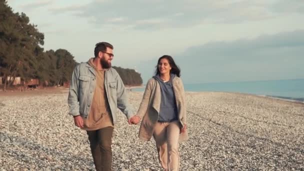 Relajado hombre está caminando en la orilla del mar con su amada esposa, sosteniendo su mano — Vídeos de Stock