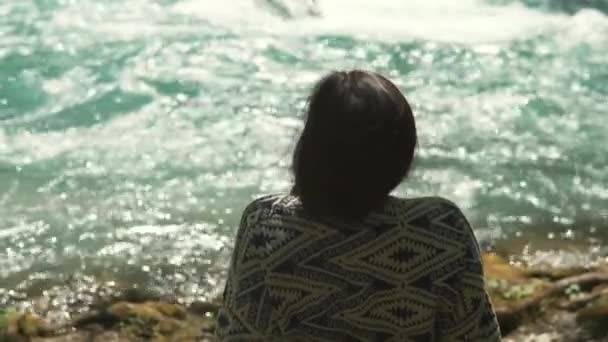 Pensive fille est assis près de la rivière dans la journée ensoleillée, vue de son dos — Video