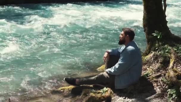 Bonito homem está descansando na margem do rio na floresta sozinho — Vídeo de Stock