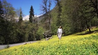 Genç kadın üzerinde yeşil bir alana çiçek açan çiçekler ile bir yaz gününde yürür