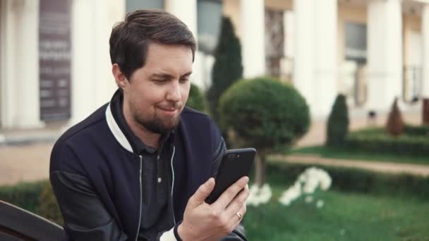 Hombre adulto está utilizando videollamadas por teléfono inteligente, sentado al aire libre — Vídeos de Stock